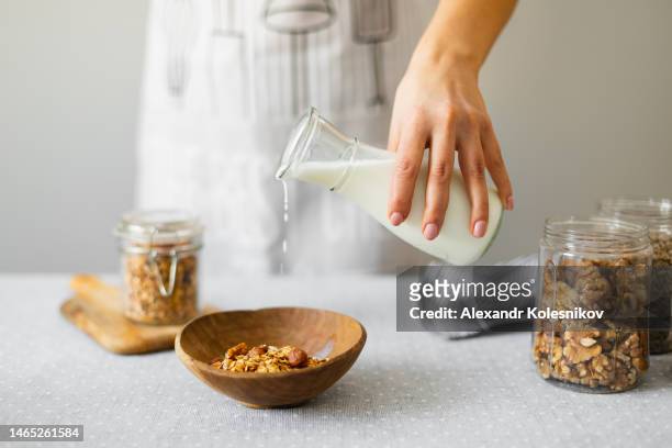 woman in apron pouring milk into a bowl with homemade granola for a delicious breakfast - pouring cereal stock pictures, royalty-free photos & images