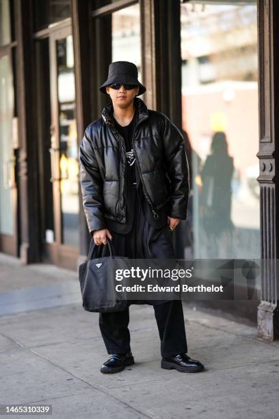 Guest wears a black nylon bob, black sunglasses, gold earrings, a gold chain necklace, a black t-shirt with white logo from Prada, a black shiny...