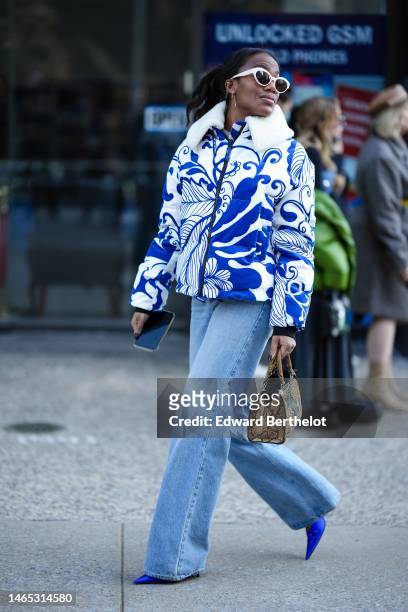 Guest wears white latte sunglasses, a white and royal blue print pattern with white sheep collar zipper coat, blue faded denim wide legs pants, a...