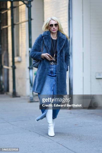 Guest wears gold sunglasses, gold earrings, a navy blue embossed wool pattern t-shirt, a blue fluffy long coat, a blue shiny leather shoulder bag...