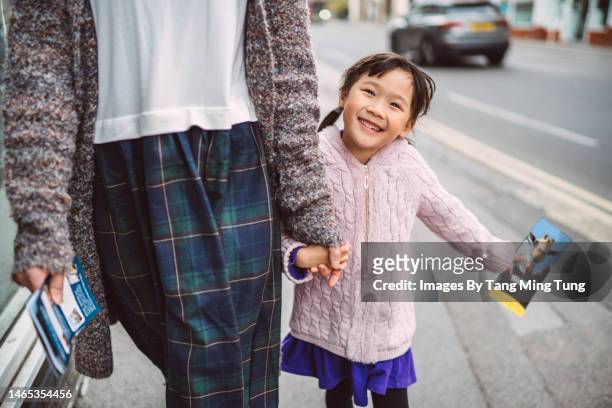 lovely cheerful girl with a tourist leaflet walking in street joyfully while exploring in town with her mom - day in the life stock pictures, royalty-free photos & images