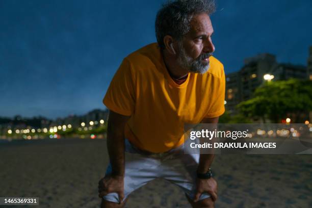 senior athlete exercising at night - hand op knie stockfoto's en -beelden
