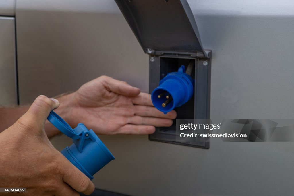 Close up, human hand plugging electric vehicle