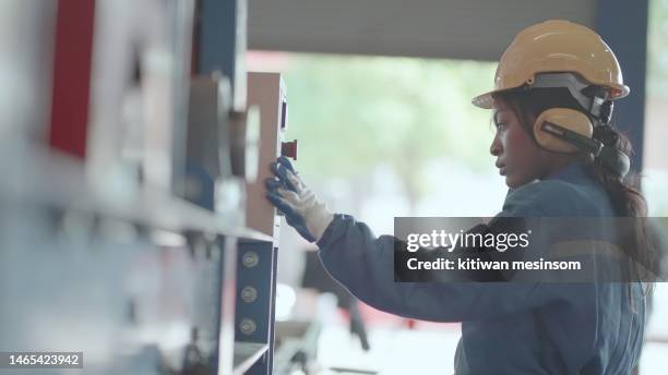 female african american industrial engineer or technician working in metal manufacturing factory or heavy industry. production line worker wear safety uniform working, hard hat and ear muff, adjust machine settings in production. - ear muffs stock pictures, royalty-free photos & images