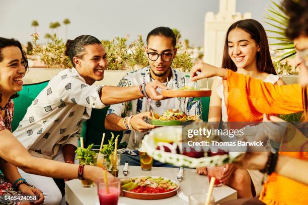 medium shot of smiling friends sharing food at rooftop restaurant - medium group of people fotografías e imágenes de stock