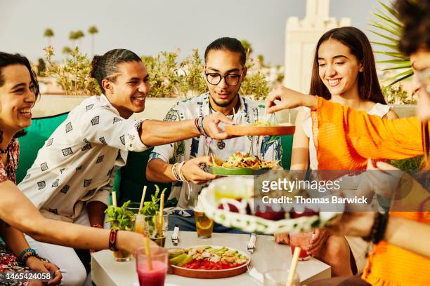 medium shot of smiling friends sharing food at rooftop restaurant - dish networks stock pictures, royalty-free photos & images