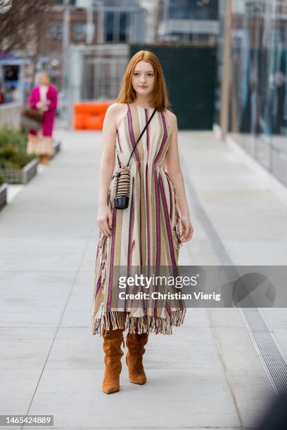 Guest wears tailored cut out striped fringed beige red brown dress, bag, wild leather boots outside Ulla Johnson during New York Fashion Week on...