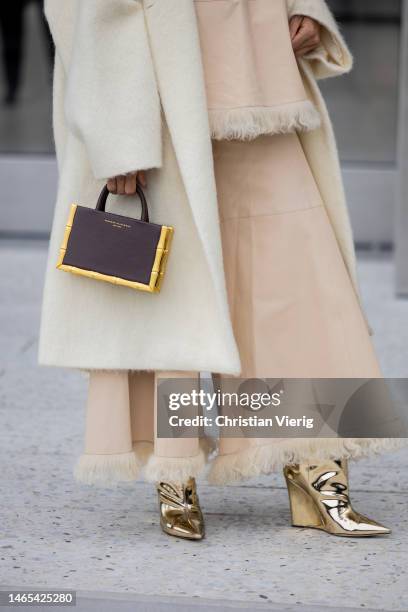 Sai De Silva wears sunglasses, earrings, wide leg flared fringes beige pants, creme white coat, brown bag, golden boots outside Ulla Johnson during...