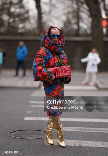 Denisa Palsha is seen wearing a Dolce & Gabbana red, blue and lilac flower midi dress and matching puffer jacket, a Dolce & Gabbana red clutch bag,...