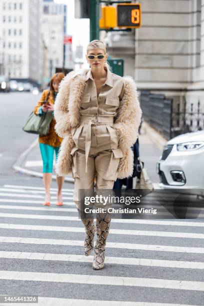 Devon Windsor wears beige button up jacket, pants with side pockets, animal print knee high boots, fleece fur coat outside Puppets & Puppets during...