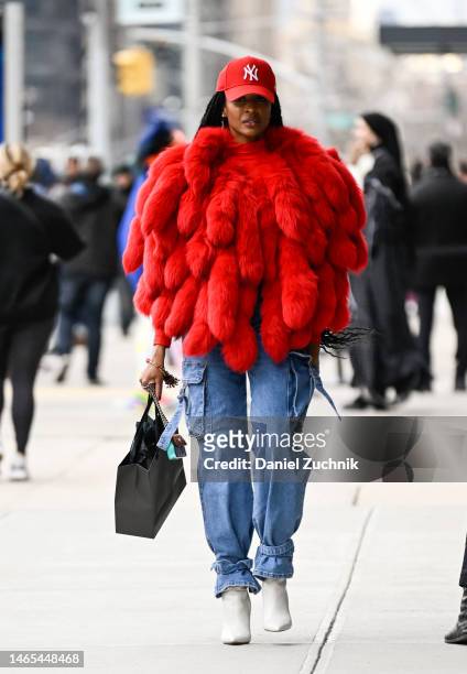 Guest is seen wearing a red faux fur coat, Yankees hat, blue jeans and white boots outside the Chiara Boni show during New York Fashion Week F/W 2023...