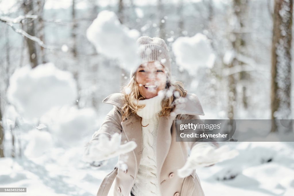 Unbeschwerte Frau, die in der Natur Schnee in Richtung Kamera wirft.