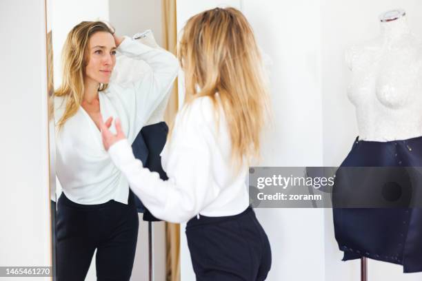 smiling woman looking at her reflection in the mirror, feeling proud of her newly designed blouse - white blouse imagens e fotografias de stock