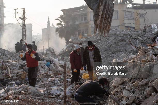 Workers stand on top of a collapsed building as a digger works its way through the debris on February 13, 2023 in Hatay, Turkey. A 7.8-magnitude...