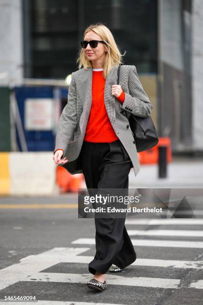 Lisa Aiken wears black sunglasses, a white t-shirt, a neon red wool pullover, a black and white small checkered print pattern wool blazer jacket, a...