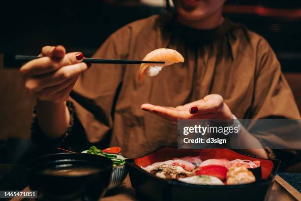 close up shot of young asian woman eating fresh nigiri sushi with chopsticks, served with miso soup and salad on the side in a traditional japanese restaurant. asian cuisine and food concept. eating out lifestyle - maki sushi stock-fotos und bilder