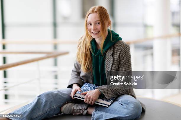 teenage school girl sitting on desk - sólo una adolescente fotografías e imágenes de stock