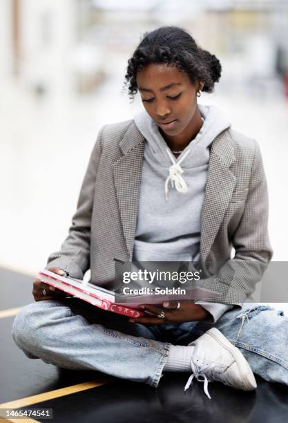 teenage girl sitting on table in school, reading - black teenage girl stock pictures, royalty-free photos & images