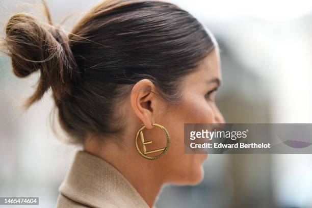 Guest wears black sunglasses from Prada, gold earrings from Fendi, a gold large chain with logo necklace from Dior, gold necklaces, a beige linen...
