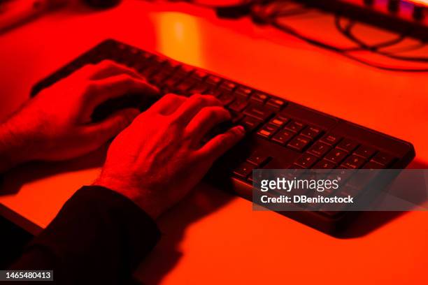 hands of a person typing and stealing information on a computer keyboard, illuminated with red light. concept of cybersecurity, theft, hacker, identity and crime. - android malware stock pictures, royalty-free photos & images