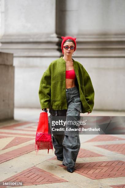 Guest wears a red wool beanie with cat ears, a gold large chain necklace, a red shoulder-off / cropped top, a green fluffy oversized jacket, dark...