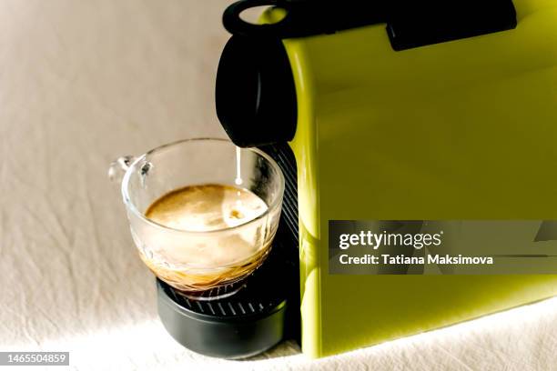 a green capsule coffee maker is on the table. coffee pours into a mug. - coffee capsules stock-fotos und bilder