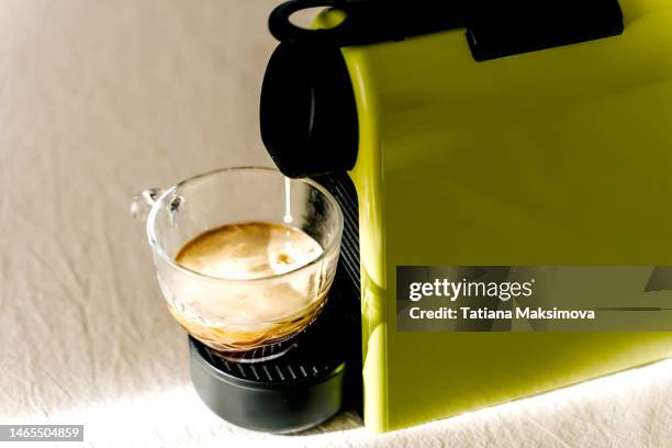 a green capsule coffee maker is on the table. coffee pours into a mug. - coffee capsule stock pictures, royalty-free photos & images