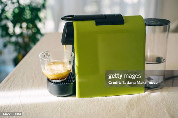 a green capsule coffee maker is on the table. coffee pours into a mug. - single serve coffee maker stock pictures, royalty-free photos & images