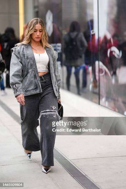 Guest wears a gold chain necklace, a white zipper cropped top, a gray faded denim oversized jacket, dark gray denim ripped large pants, a black shiny...