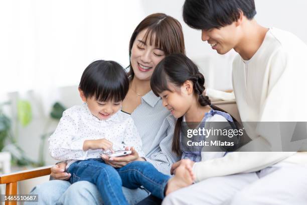 a family sitting on the sofa and looking at a smartphone - only japanese stock-fotos und bilder