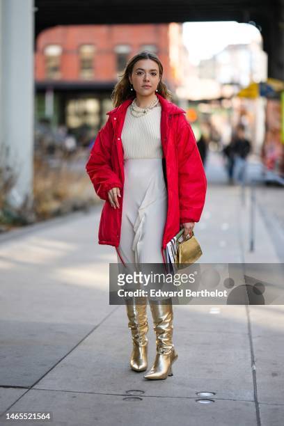 Guest wears glasses, gold earrings, gold piercings, a white pearls necklace, a beige ribbed pullover, a beige ruffled silk long skirt, a red coat, a...