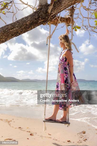 best ager woman stands on a tree swing, enjoys the beach in martinique and looks into the distance of the ocean - best ager woman stockfoto's en -beelden