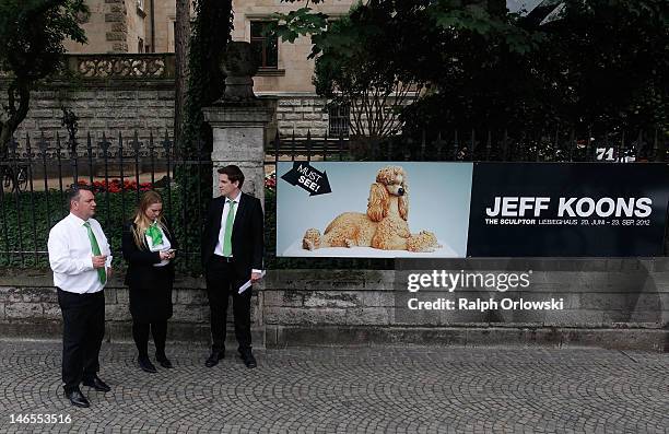 Employees stand next to a placard of the exhibition 'Jeff Koons. The Painter & The Sculptor' at the Liebighaus museum on June 19, 2012 in Frankfurt...