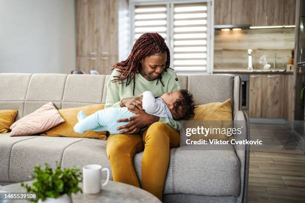caring black mother looking after her little baby boy while he is asleep - mum sitting down with baby stockfoto's en -beelden