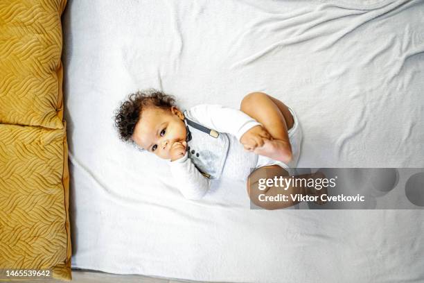 cute little baby boy lying down on a stretched out blanket after having his diaper changed, while sucking his right hand thumb and holding his left feet in other hand - feet sucking stock pictures, royalty-free photos & images