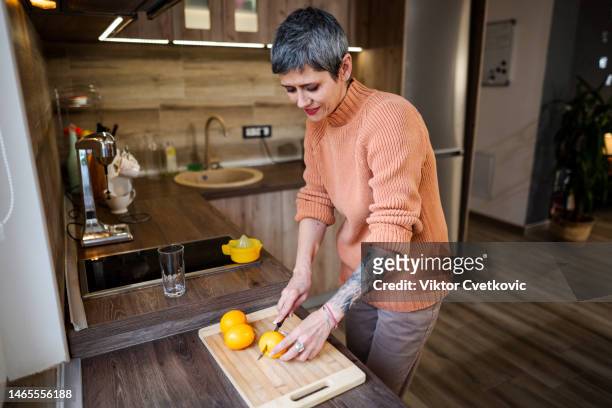 mature woman with forearm tattoo cutting fresh lemons for lemonade - short hair cut stock pictures, royalty-free photos & images