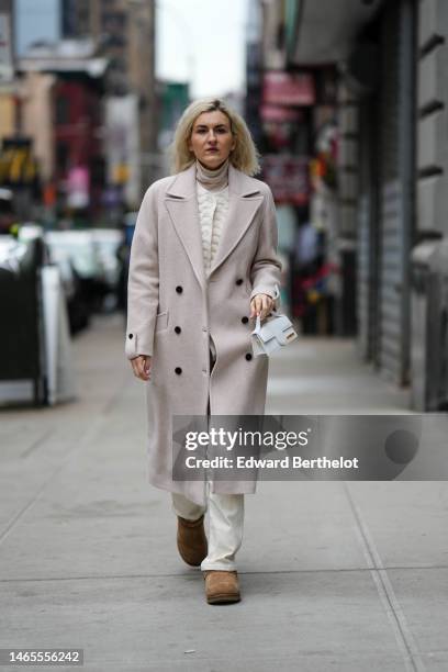 Guest wears a beige turtleneck pullover, a white embossed pattern buttoned jacket, a beige long coat, a white shiny leather handbag from Jacquemus,...