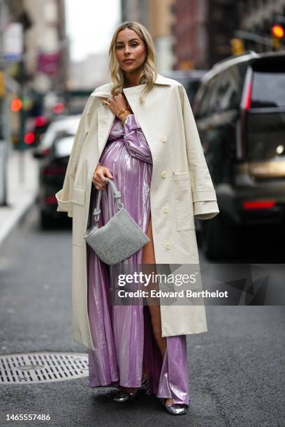 Guest wears a gold Juste Un Clou bracelet from Cartier, gold bracelets, rings, a white latte shiny leather crocodile print pattern long coat, a...