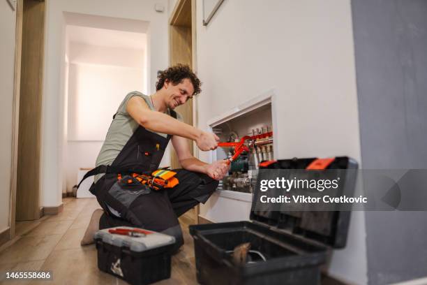 lächelnde reparaturarbeiter beheben ein problem mit fußbodenheizungsrohren - rohrbruch stock-fotos und bilder