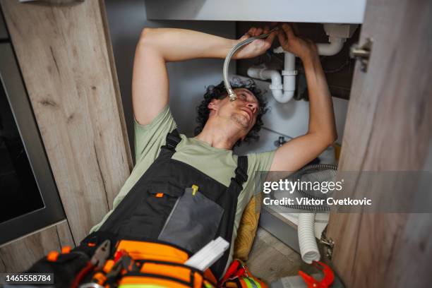 plumber fixing a problem with water pipes under kitchen sink - looking under sink stock pictures, royalty-free photos & images
