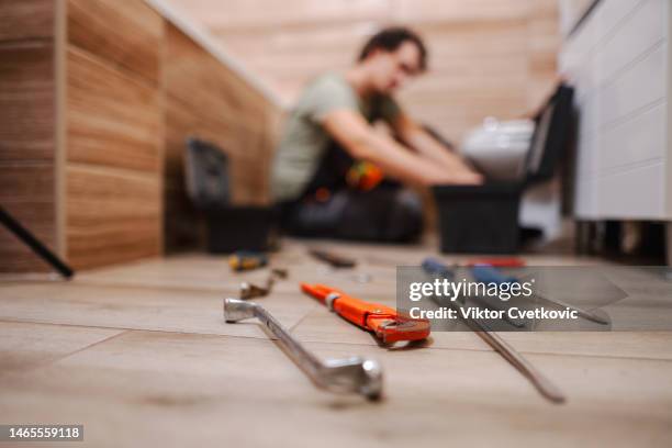 work tools lying on bathroom floor while plumber is fixing a problem with toilet in the background - plumbing tools stock pictures, royalty-free photos & images