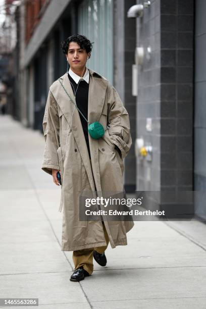 Guest wears a white shirt, a black wool pullover, a beige oversized long coat, a green shiny leather embossed checkered pattern crossbody bag, brown...