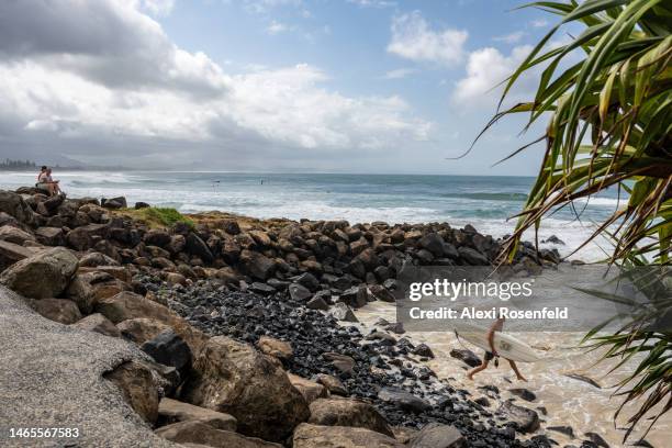 Surfer leaps across rocks to enter the ocean at Main Beach on February 13, 2023 in Byron Bay, Australia. Byron Bay, NSW is the easternmost point of...
