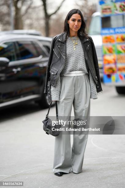 Guest wears diamonds earrings, gold long chain pendant necklaces, a pale gray braided wool pullover, a black shiny leather zipper biker jacket, pale...