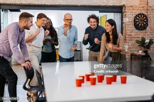 colleagues playing beer pong at the office - beer pong stock pictures, royalty-free photos & images