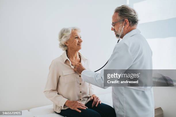 doctor listening to senior woman patient heartbeat - pulse trace stockfoto's en -beelden