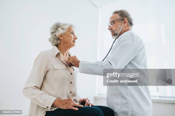 doctor listening to senior woman patient heartbeat - cardiologist stock pictures, royalty-free photos & images