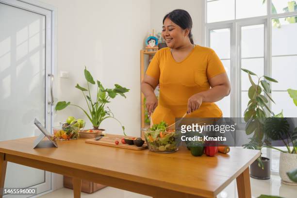 plus size woman using digital tablet to learning how to make salads and healthy foods teach by social media. - nutritionist stock pictures, royalty-free photos & images