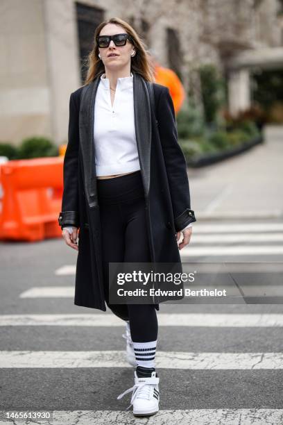 Guest wears black sunglasses, a white high neck polo shirt, a black long coat, black legging pants, white socks, white leather and black logo print...