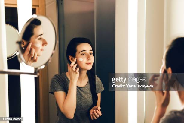 young beautiful israeli woman with clean white skin is applying moisturizer and doing face massage - facial moisturizer stock pictures, royalty-free photos & images